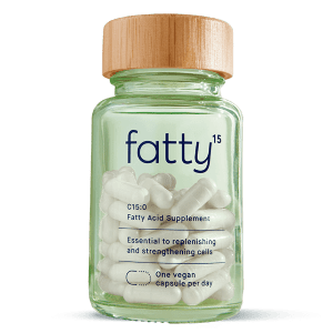 A clear glass jar with a wooden lid labeled "fatty15" contains white capsules, described as a vegan fatty acid supplement with instructions for daily use.